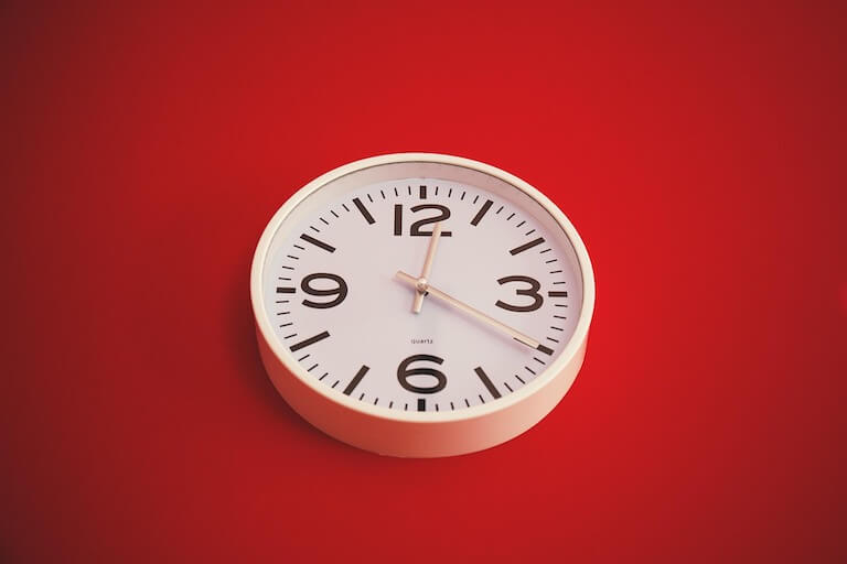 Weisse analoge Uhr an roter Wand.